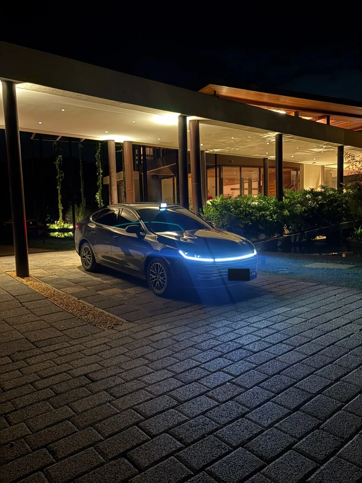 BYD King preto com os faróis acesos na entrada de um hotel à noite
