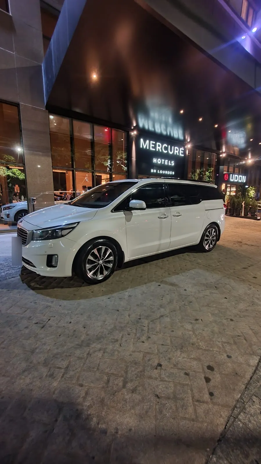 Kia Carnival branca na porta de um hotel à noite